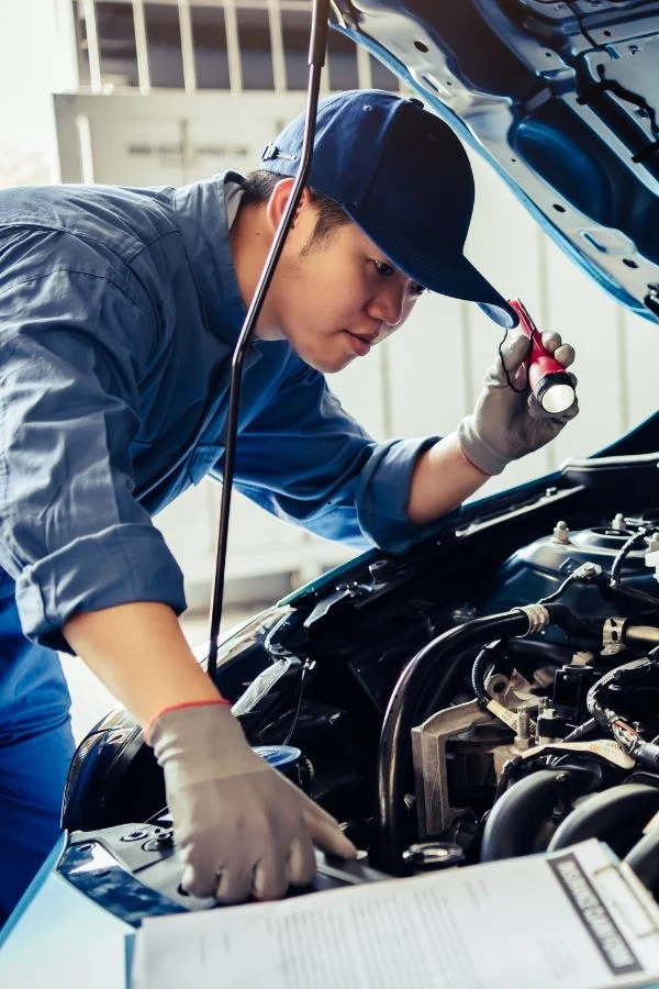 Mechanic in a cap shining a torch into a car's engine bay